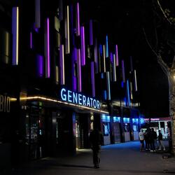 Shot of the Generator Hostel. The building is adorned with vertical LED light strips of different colors. It looks nice at night.